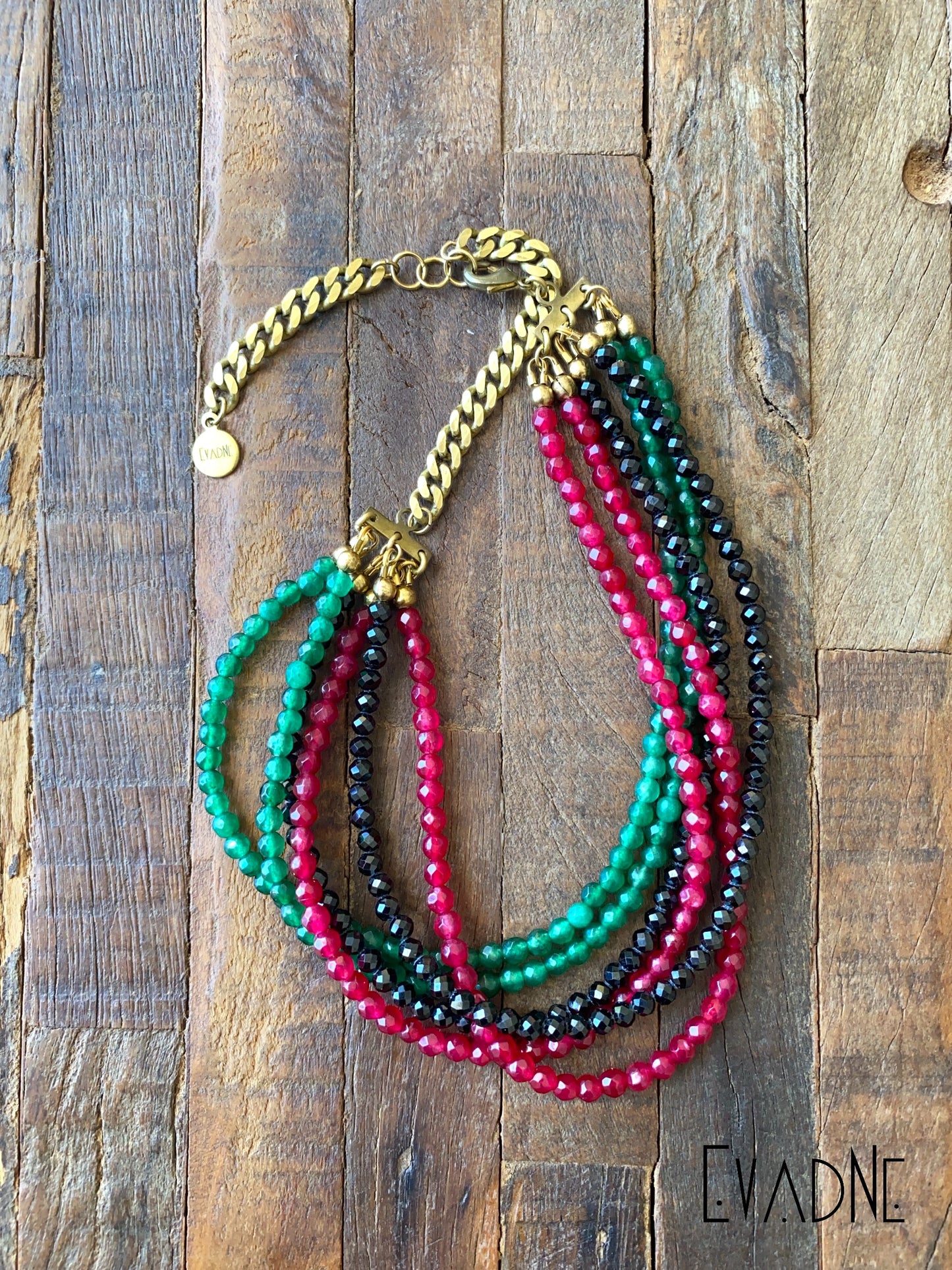 Multistrand beaded necklace with gold chain on a wooden surface, branded 'Evadne'.