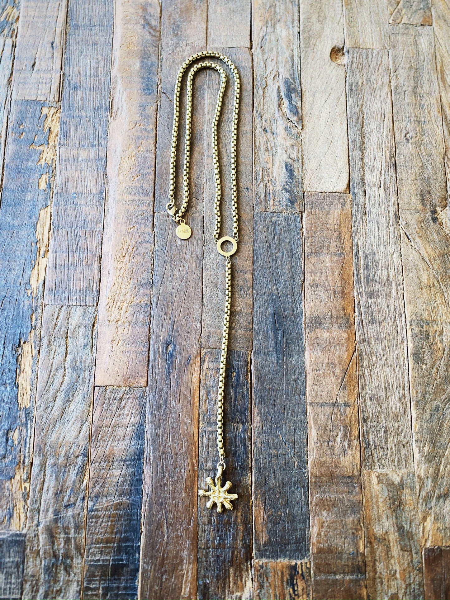 Gold necklace with an Adinkra charm on a wooden surface