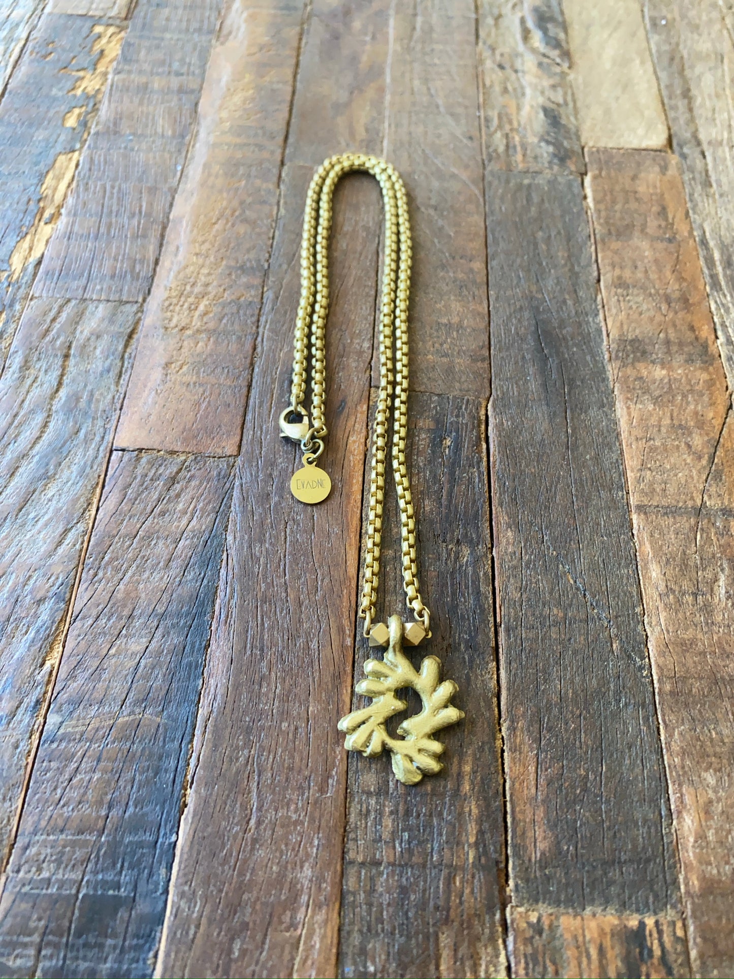 Gold necklace with an Adinkra Bi Nka bi pendant on a wooden surface