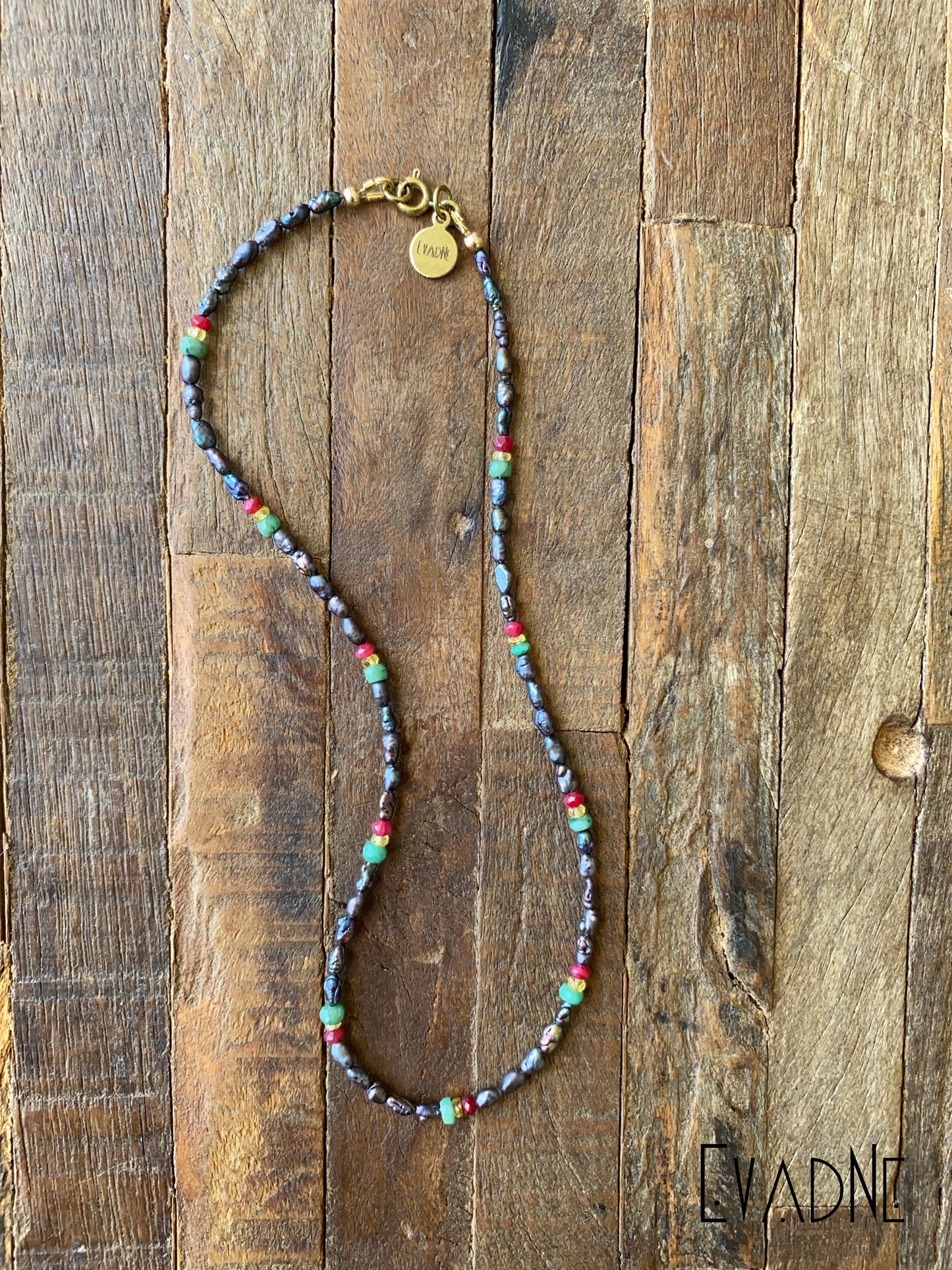 Beaded necklace with colorful beads on a wooden surface, branded 'EvaDne'.