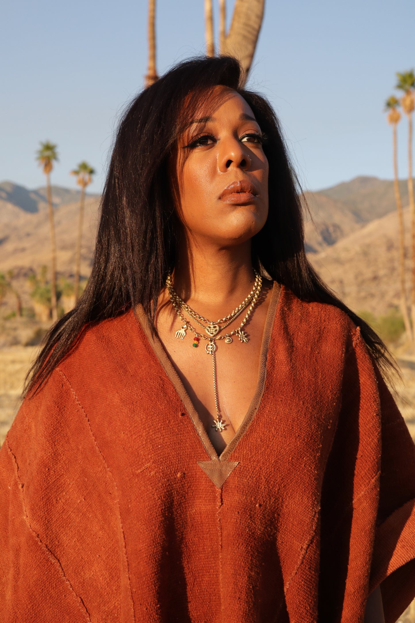 Woman wearing a terra cotta poncho with stacked brass chains with a scenic desert background