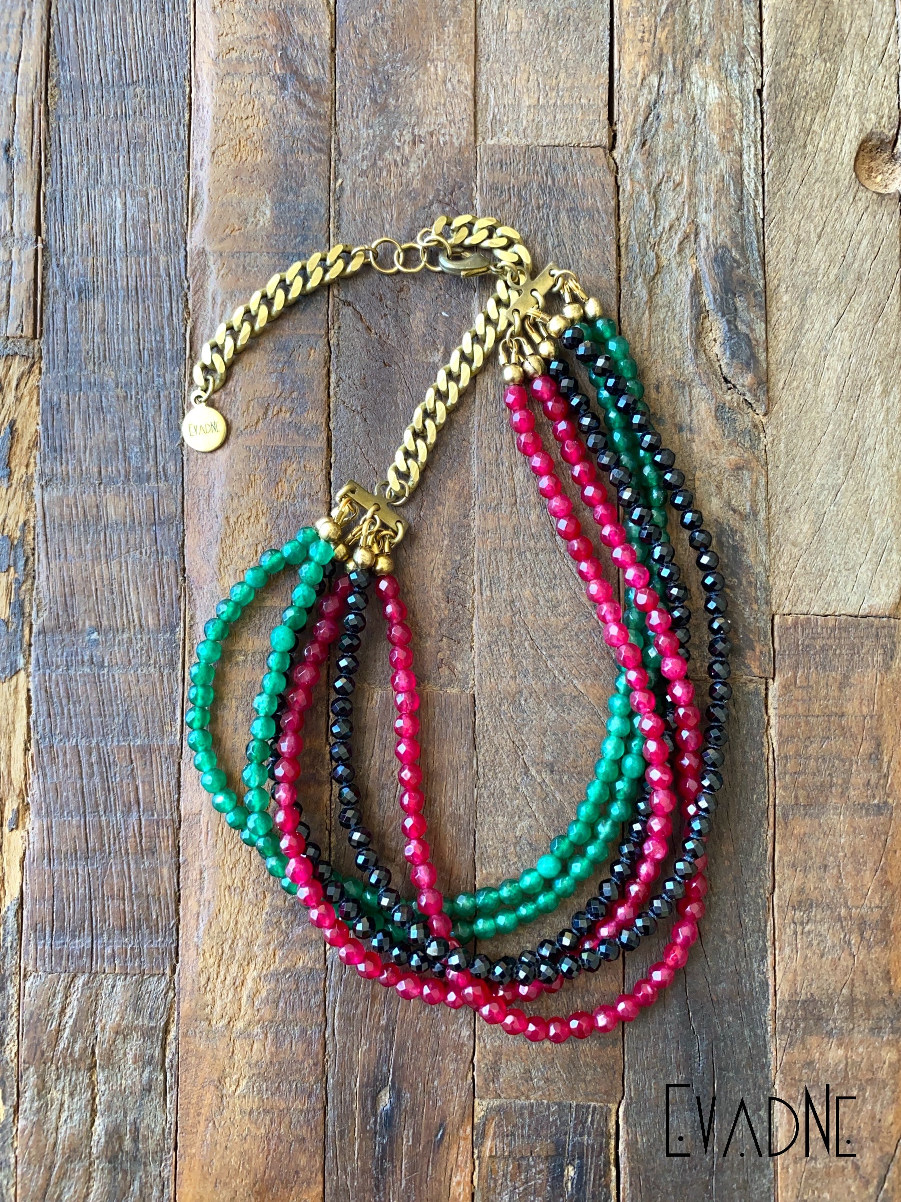 Multistrand beaded necklace with gold chain on a wooden surface, branded 'Evadne'.