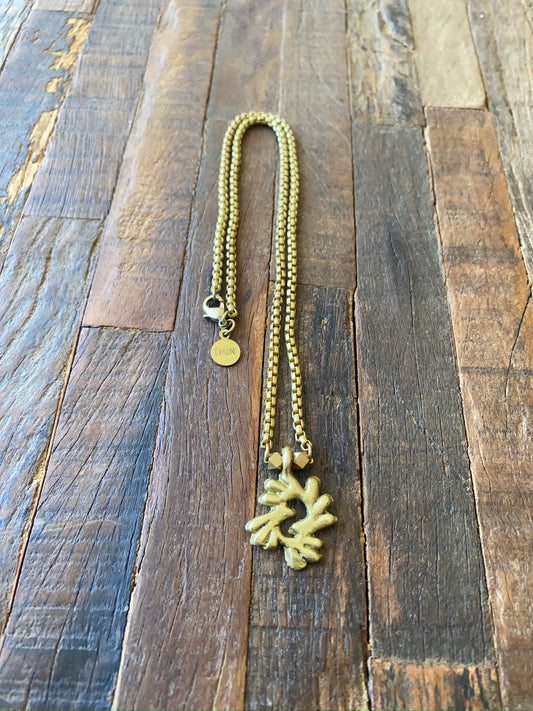 Gold necklace with an Adinkra Bi Nka bi pendant on a wooden surface