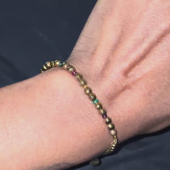 Gold hematite and multigem bracelet with Cuban link chain worn at wrist.