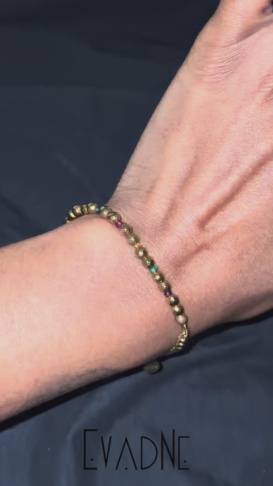 Gold hematite and multigem bracelet with Cuban link chain worn at wrist.